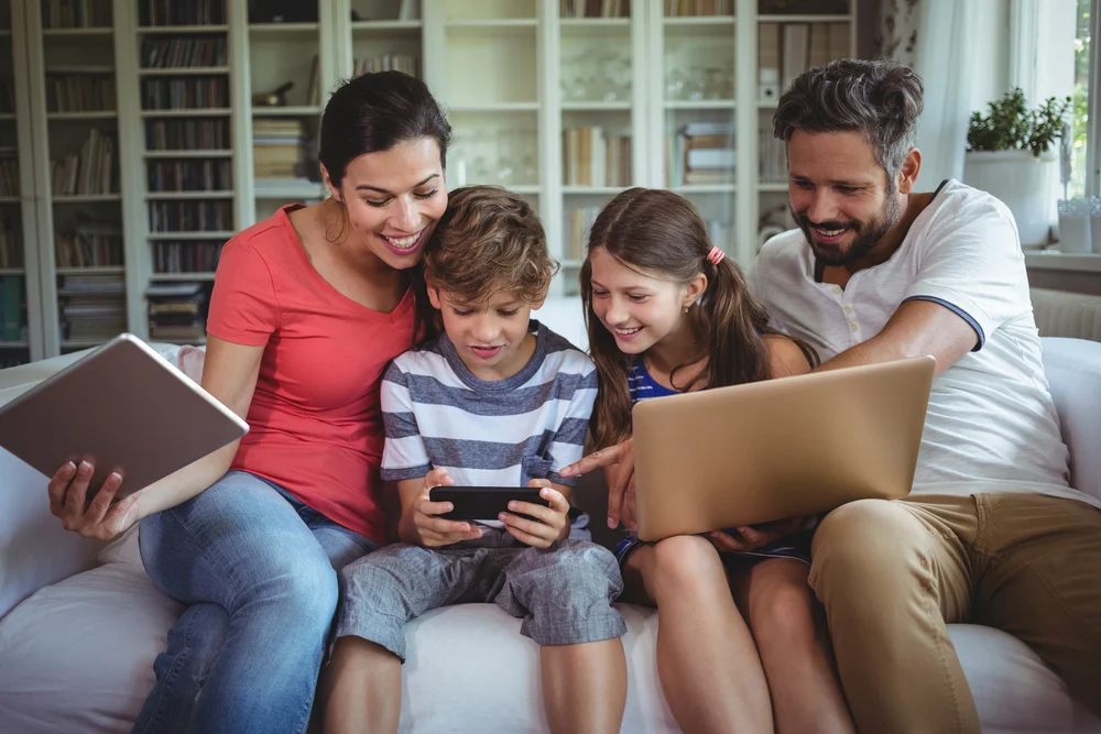 Happy family sitting on sofa and using laptop, mobile phone and digital tablet at home.